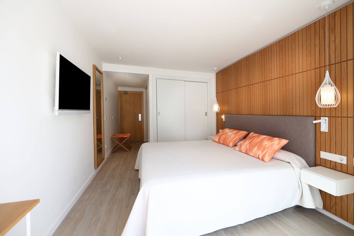 Ein modernes Schlafzimmer mit einem großen Bett, einer Wand aus Holzpaneelen und einem angebrachten Fernseher.