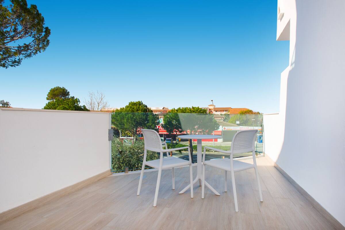 Ein Balkon mit Tisch und Stühlen, mit Blick auf eine Straße mit Gebäuden und Bäumen.