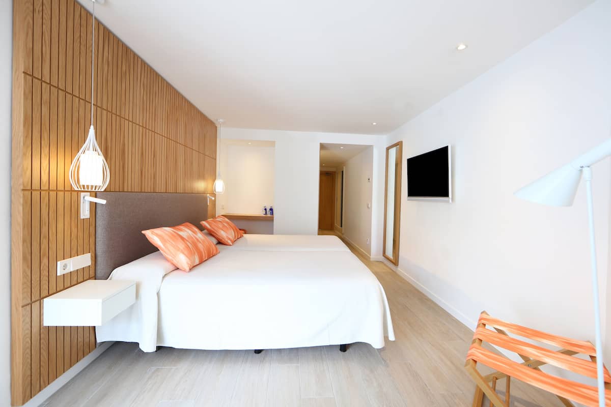 Ein modernes Hotelzimmer mit einem großen Bett, einer Wandverkleidung aus Holz, einer eingebauten Ablage, einem Nachttisch und einem an der Wand montierten Fernseher.