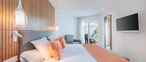 A modern hotel room with a large bed, a wooden headboard, a bedside table, a TV, and a view of the outdoors.
