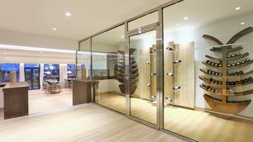 Ein modernes Interieur mit einer Glastrennung, einem Weinkühler aus Holz und einer Sitzecke mit Tischen und Stühlen.