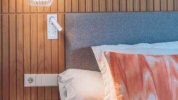 A neatly made bed with a grey headboard, a white bedside table, and a wall-mounted light fixture.
