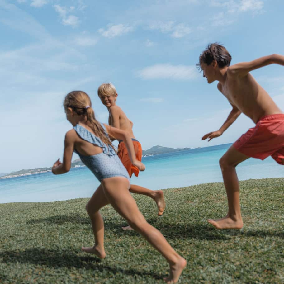 Three people running on a grassy area near a body of water.