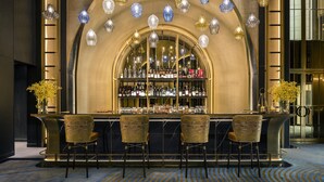 Una zona de bar con un mostrador curvo, varios taburetes y una variedad de botellas y vasos en estantes.