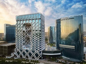 A modern building with a unique geometric facade, surrounded by other high-rise structures. - City of Dreams – Nüwa Macau (Cotai)