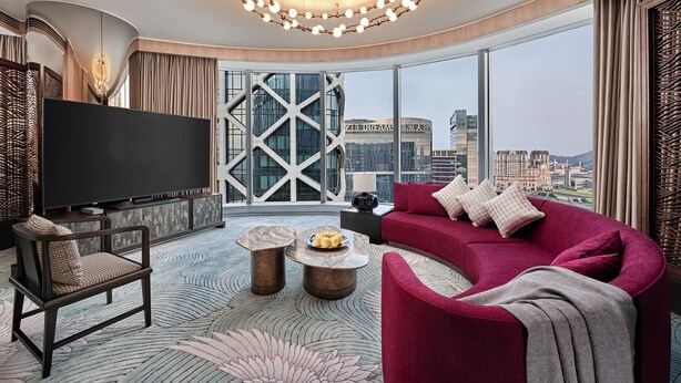 Una sala de estar moderna con un televisor grande, un sofá rojo y vistas de la ciudad a través de amplios ventanales.
