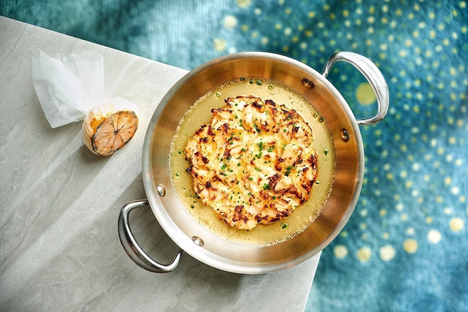 A pan with grilled chicken and a piece of bread on a marble surface.