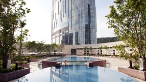 Un edificio moderno con fachada de vidrio reflectante, una piscina central y abundante vegetación.