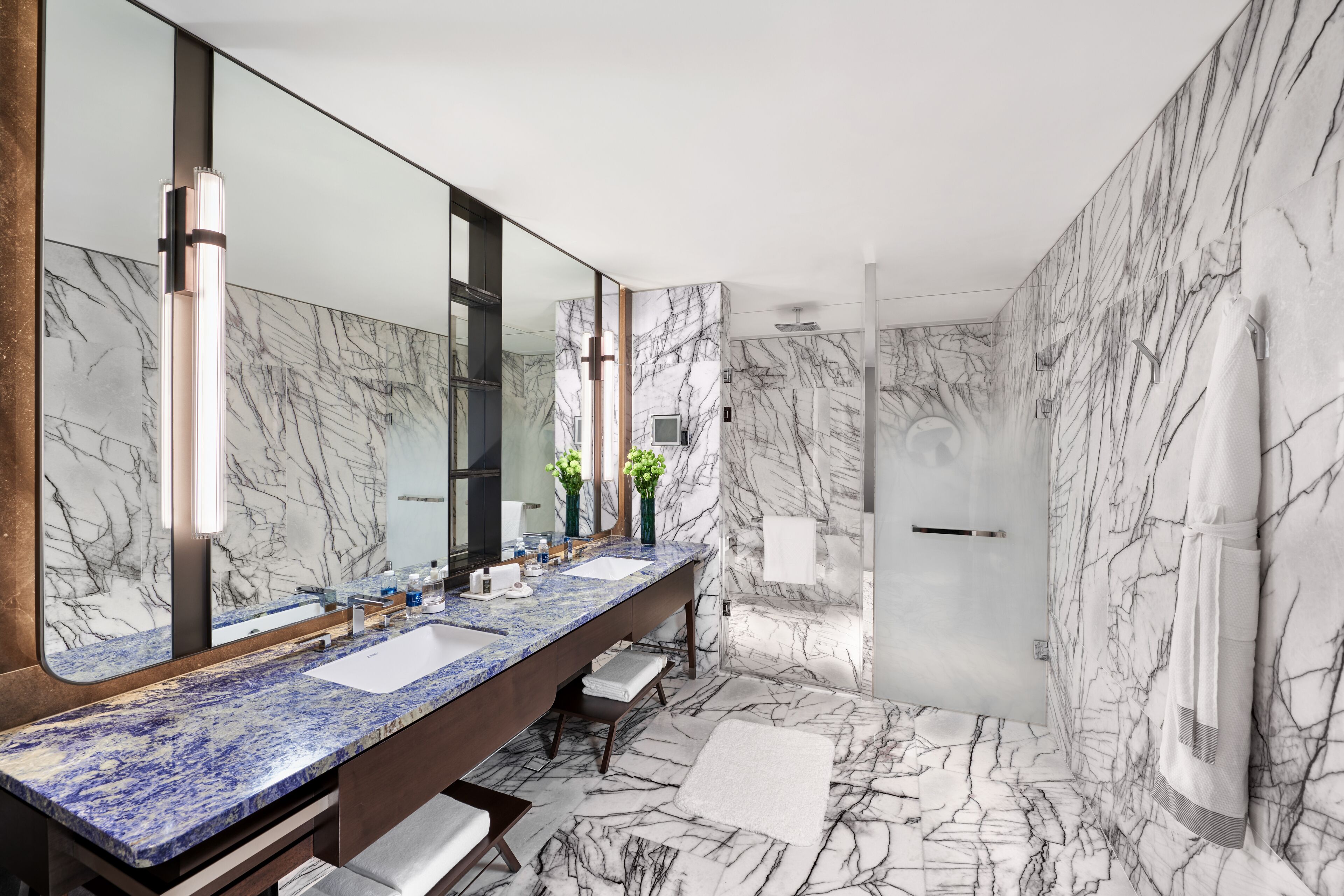 Un baño moderno con piso de mármol, un mueble de tocador espacioso con cubierta de mármol azul y un espejo grande.