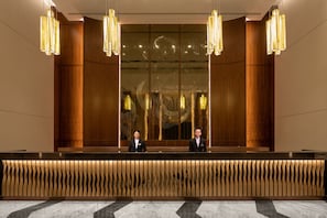A reception area with a modern design, featuring a reception desk, two staff members, and a large decorative wall. - City of Dreams – Nüwa Macau (Cotai)