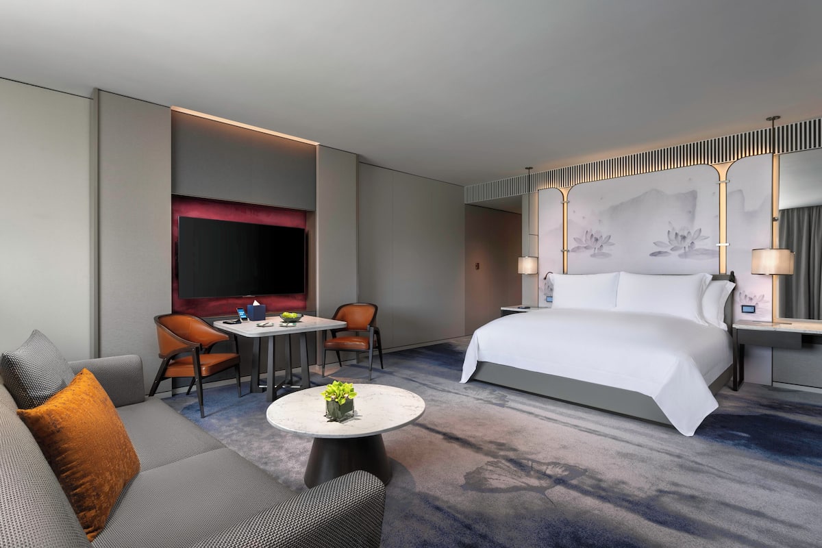 Ett modernt hotellrum med en stor säng, en soffa, två fåtöljer, ett litet bord med en växt och en tv.
