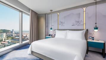 A modern hotel room with a large bed, a city view, and a desk with a phone.