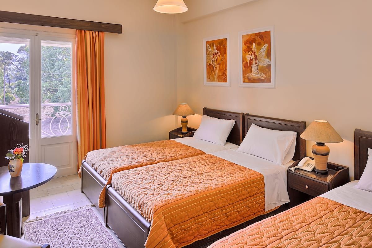 A hotel room with three beds, a small table with a vase, and artwork on the wall.