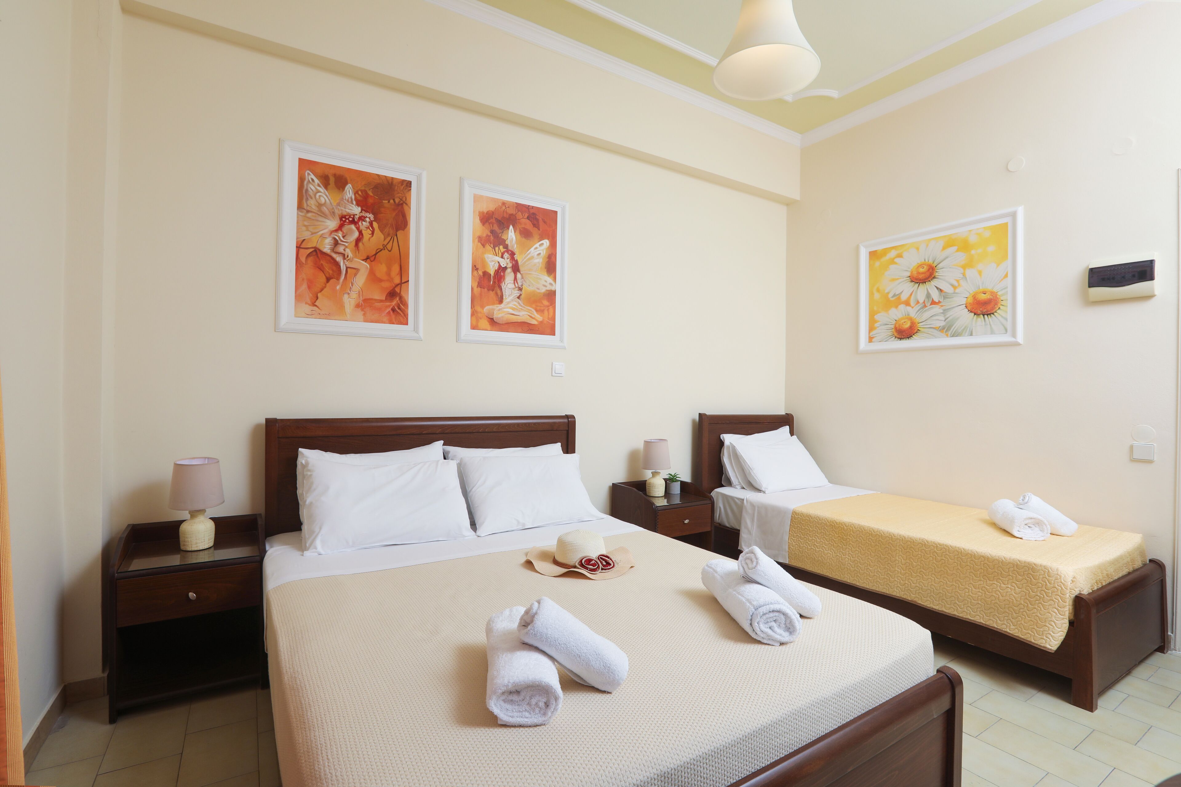 A hotel room with a large bed, two smaller beds, artwork on the walls, and a nightstand with a lamp.