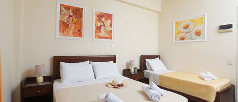 A hotel room with a large bed, two smaller beds, artwork on the walls, and a nightstand with a lamp.