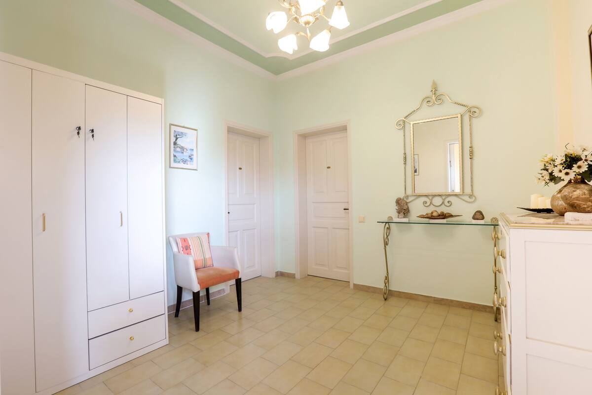 A room with a white wardrobe, a chair, a glass console table, and a mirror.