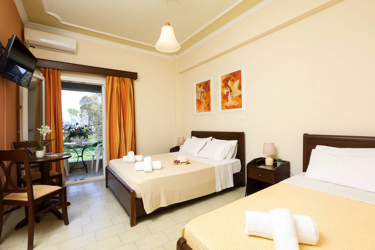 A hotel room with a bed, a desk, a chair, a TV, and a balcony with orange curtains.