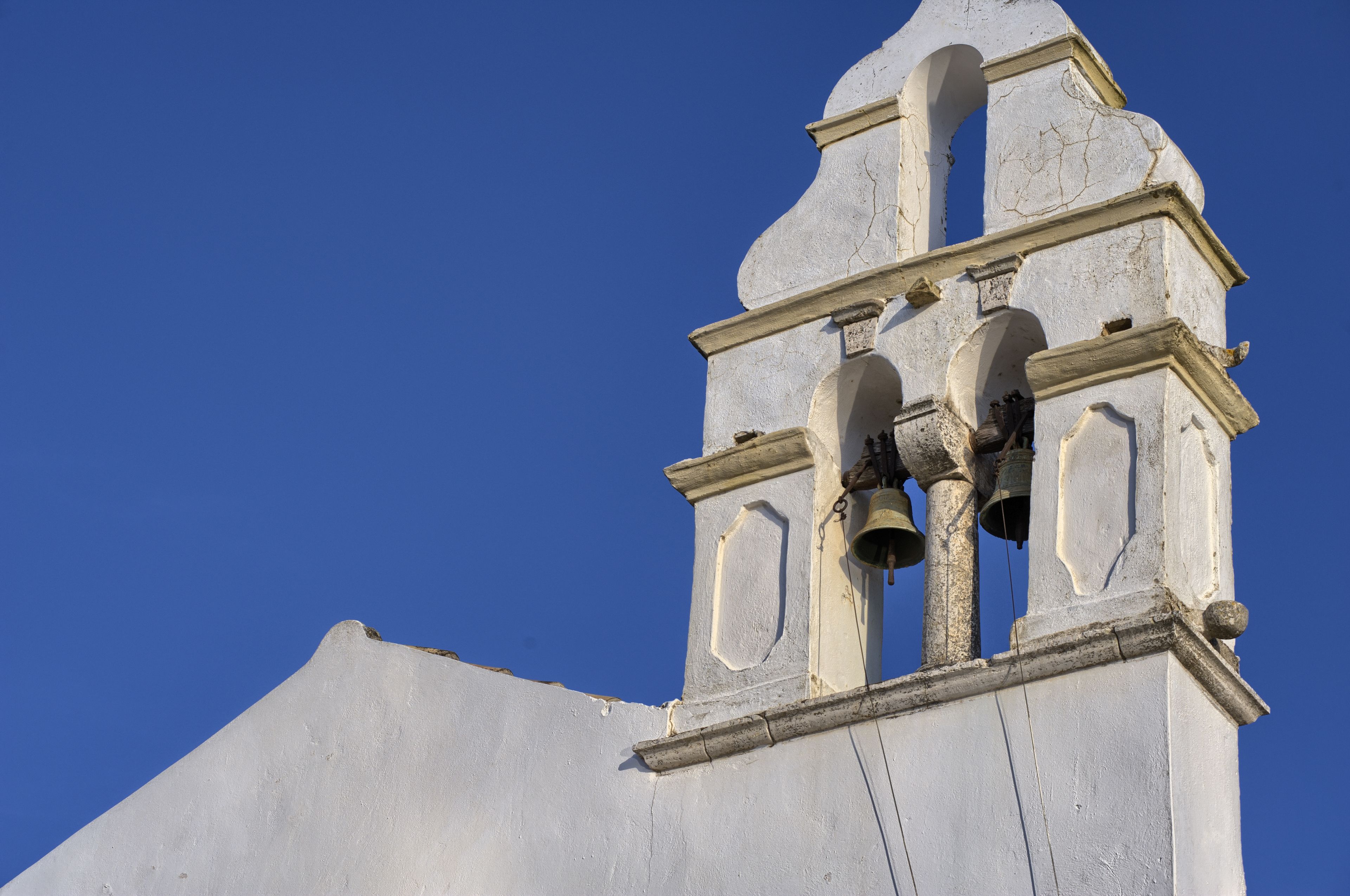 A church tower with three bells and a clear blue sky.