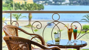 A balcony with wicker chairs and a table with two drinks and a glass of water. - Molfetta Beach Hotel (Corfu)