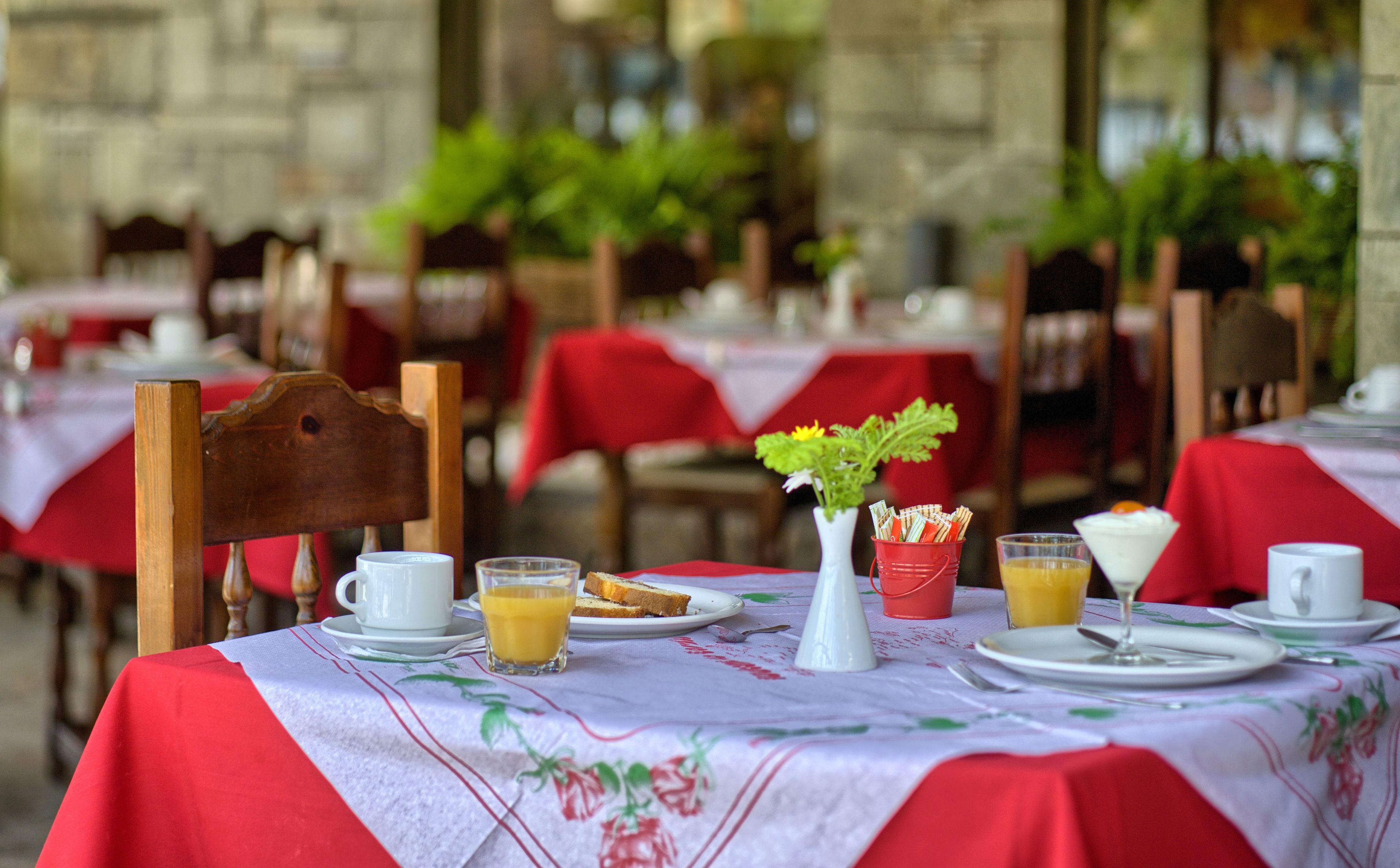 A dining table set with a white cup, a glass of orange juice, a plate with toast, a small white pitcher, and a red bucket with napkins.