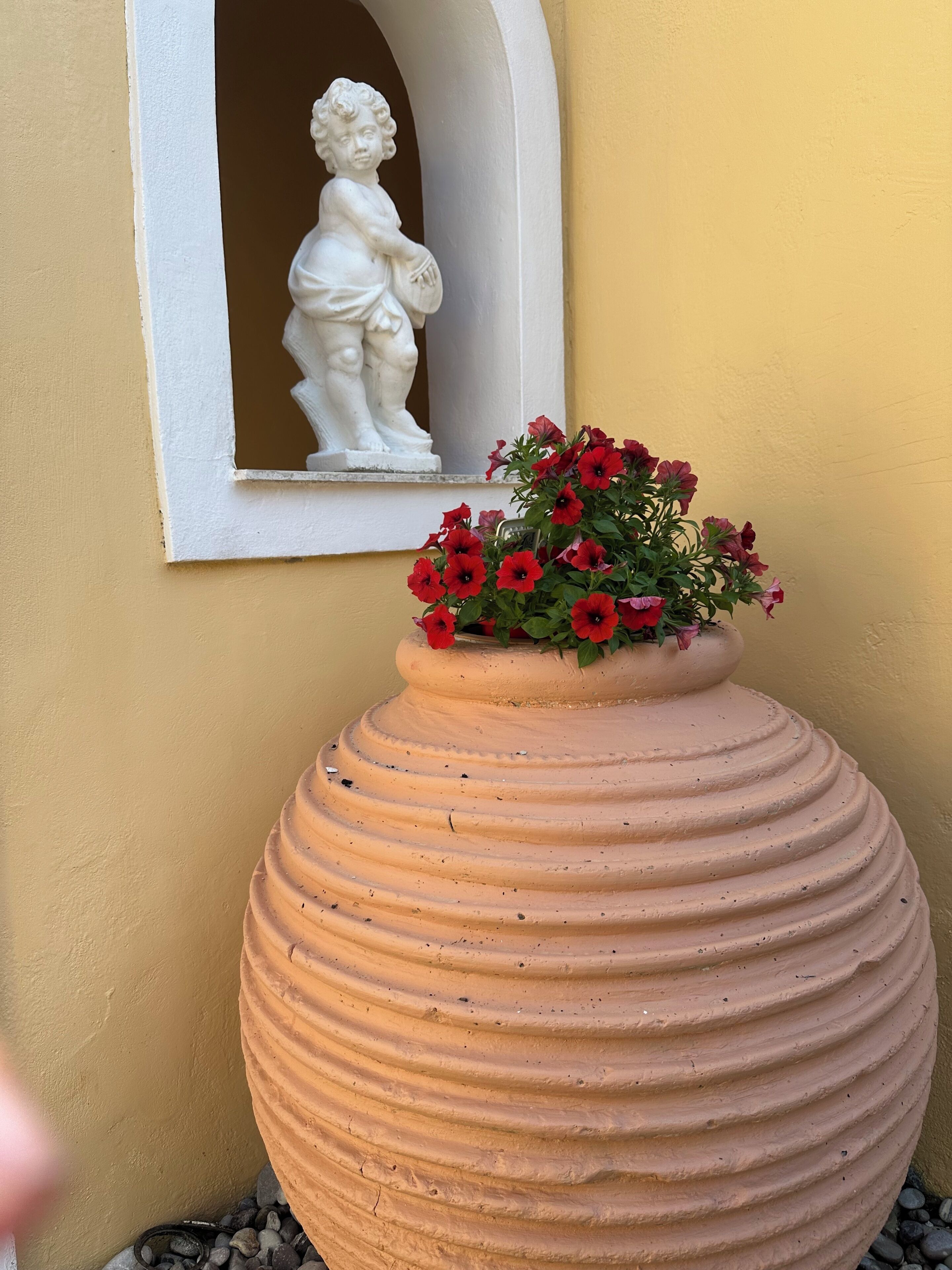 Ein großer Terrakotta-Pflanztopf mit roten Blüten, eine weiße Statue und eine gelbe Wand.