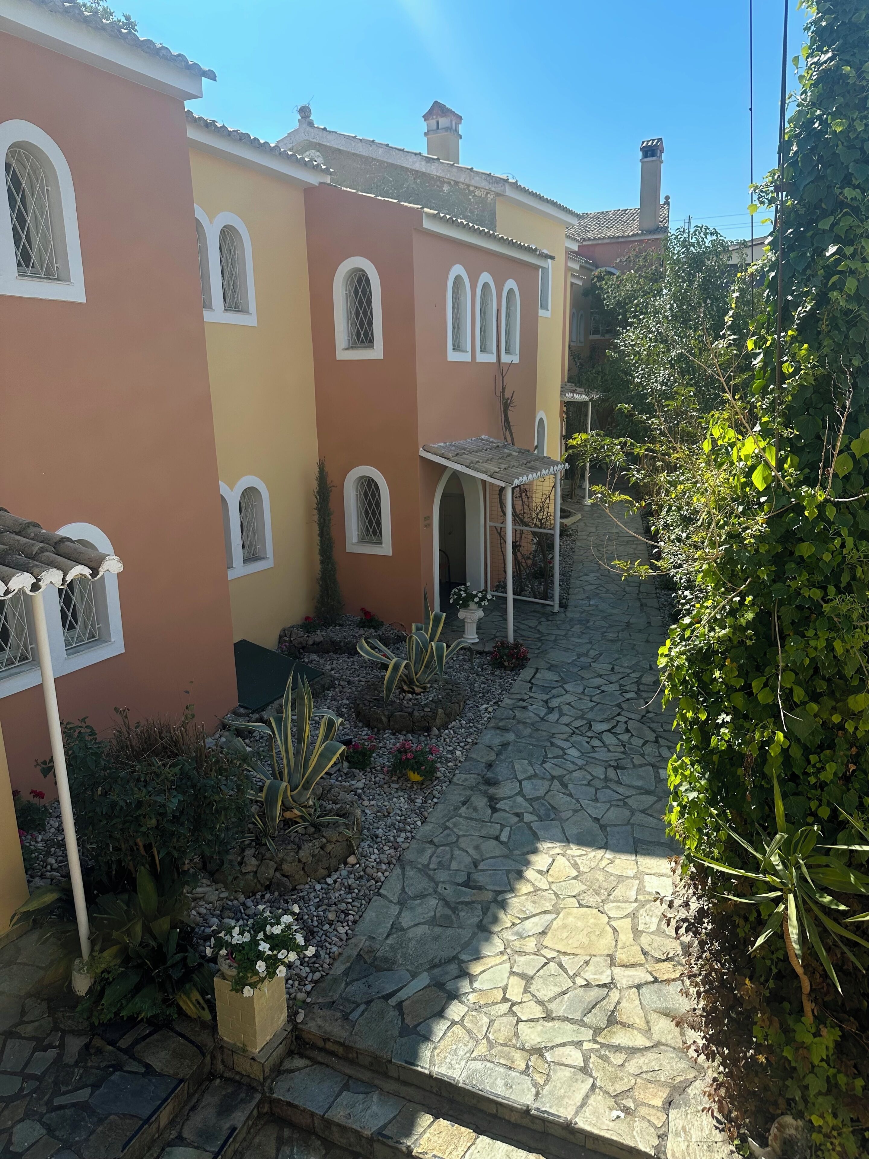 A narrow stone pathway leading to a building with arched windows and a tiled roof.
