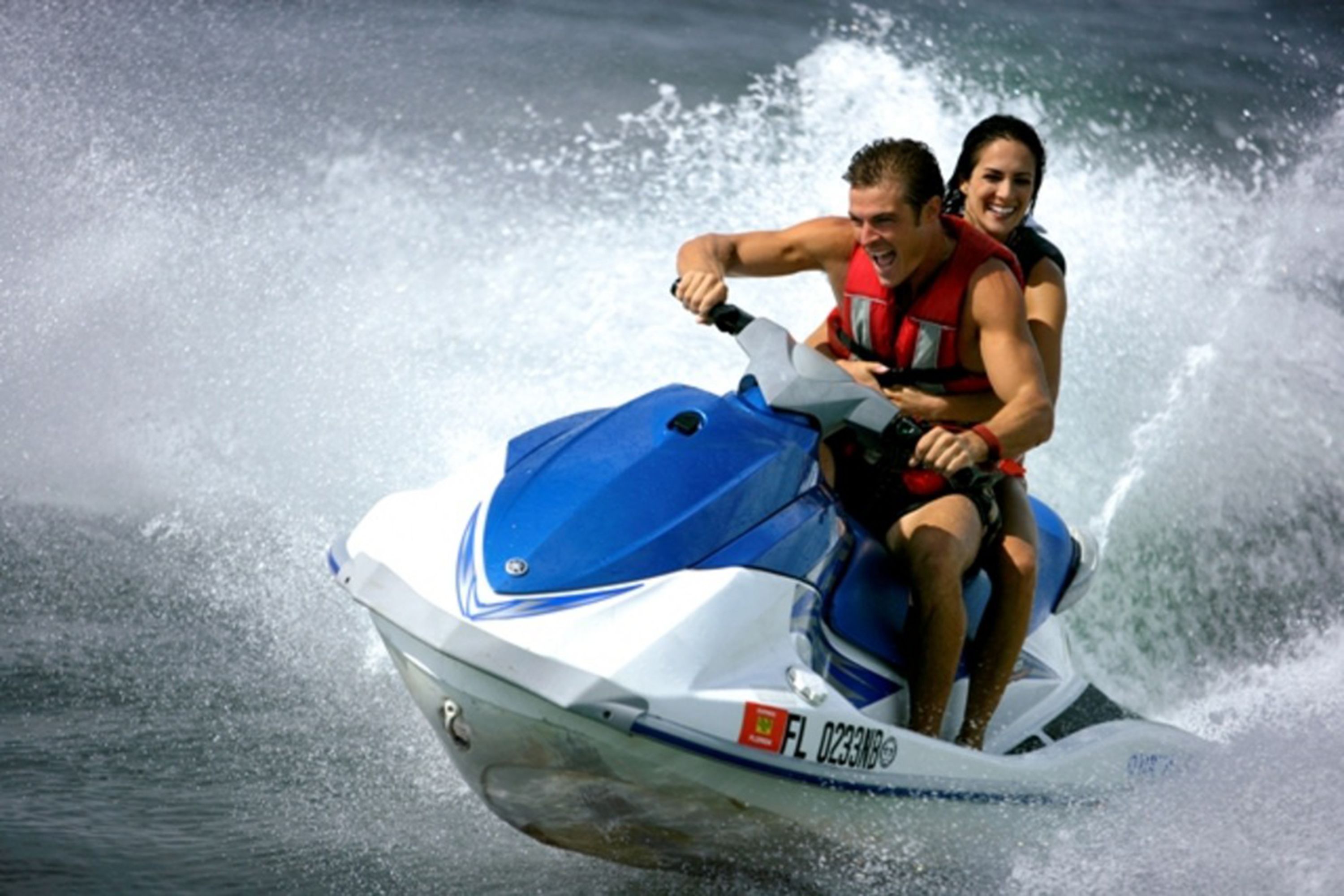 Un jet ski con dos personas, una vestida con chaleco salvavidas rojo.