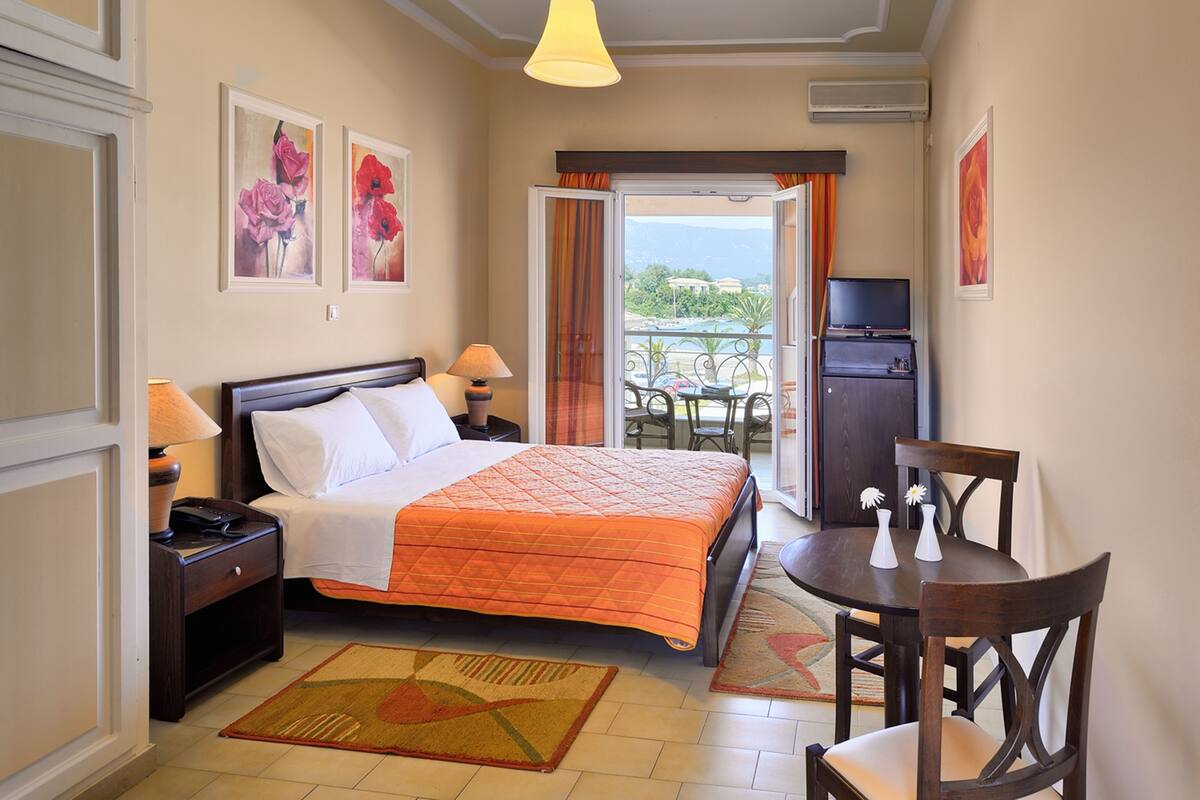 A hotel room with a bed, bedside tables, a TV, a dining table with chairs, and a view of the outdoors.