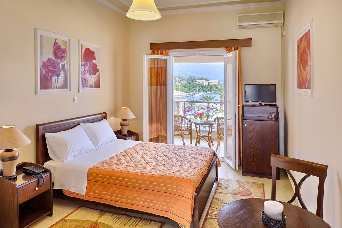 A hotel room with a bed, bedside lamps, a TV, a desk, and a balcony with a view.