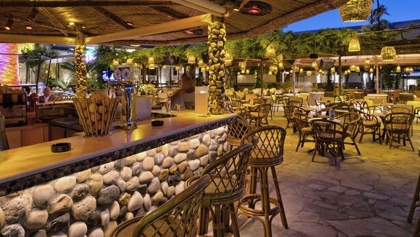 An outdoor bar area with stone walls, wicker furniture, and hanging lights. - Molfetta Beach Hotel (Corfu)