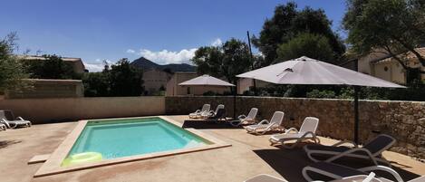 A pool area with lounge chairs and umbrellas, surrounded by stone walls and trees.