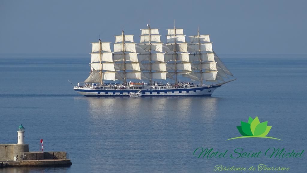 A large sailing ship with multiple masts and sails, docked at a pier with a lighthouse in the background.