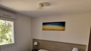 Une chambre d’hôtel avec deux lits, un tableau au mur et une fenêtre donnant sur des arbres.