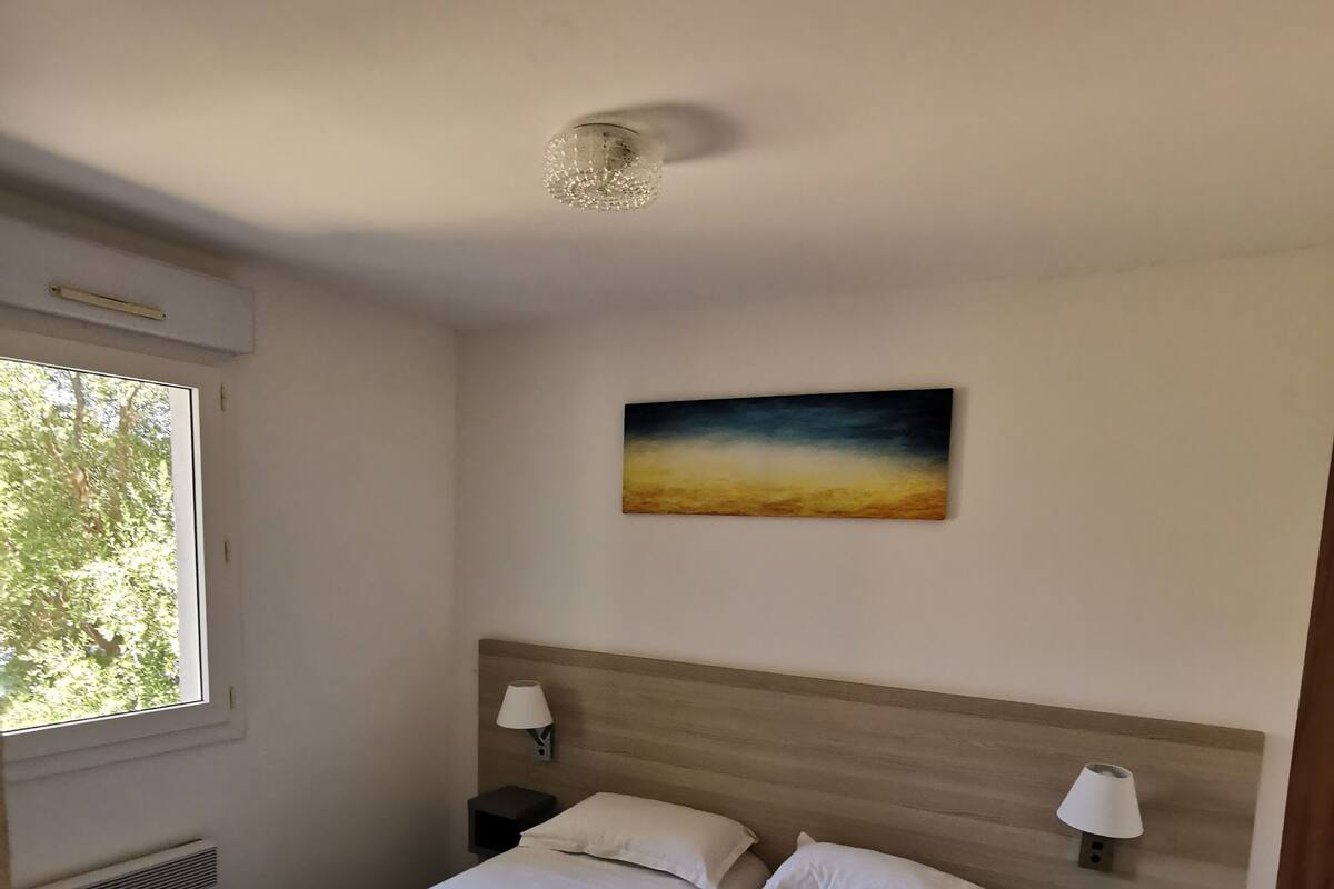 A hotel room with two beds, a painting on the wall, and a window with a view of trees.