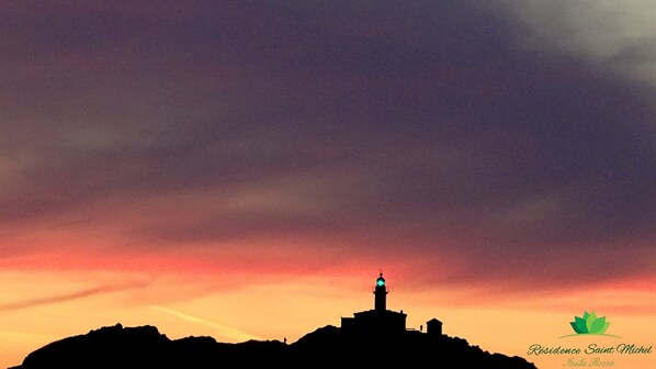 On aperçoit la silhouette d’une colline surmontée d’un phare, avec un petit bâtiment et une personne debout sur la colline.