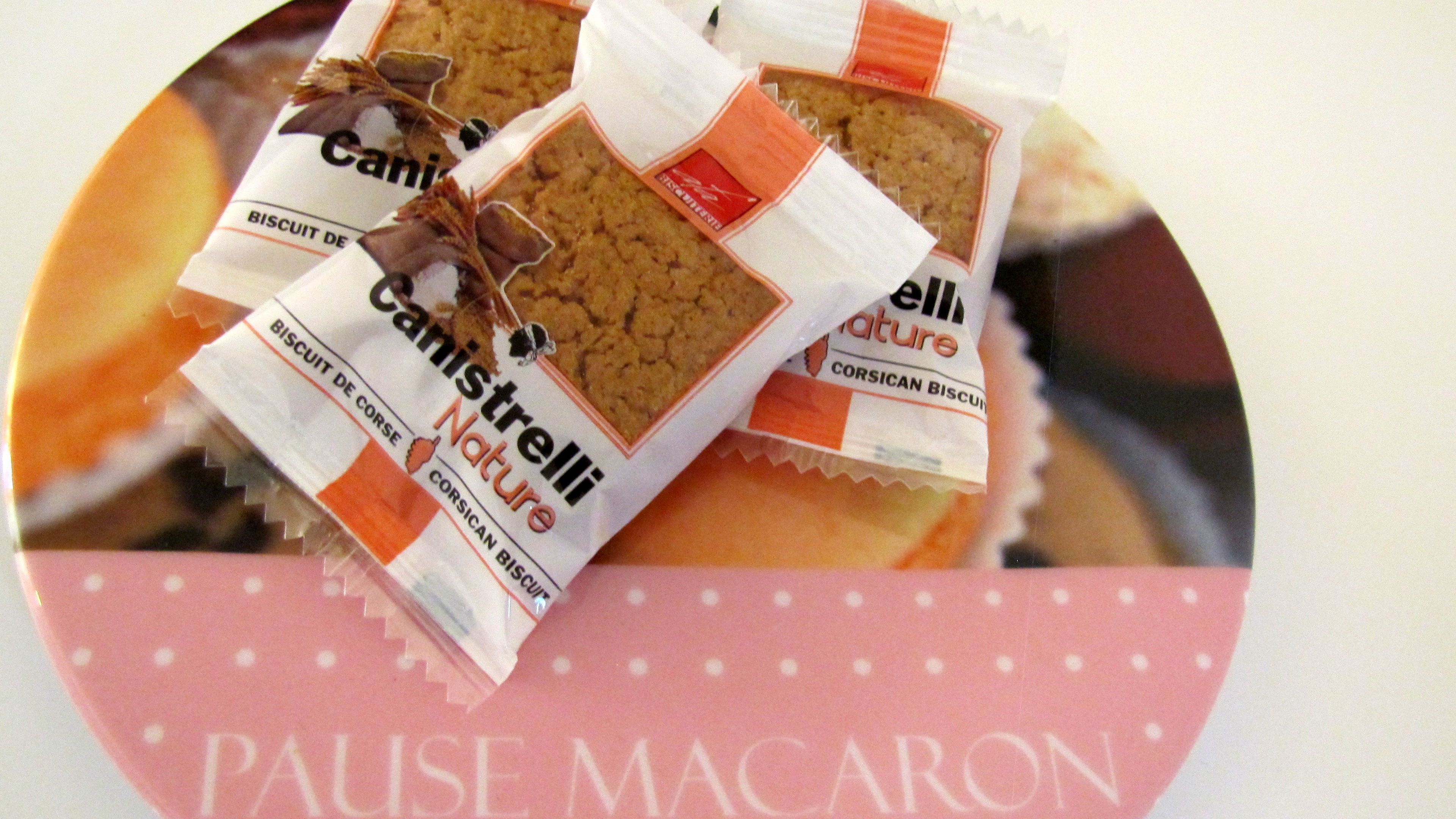 A close-up of packaged biscuits labeled "Canistrelli Nature" and "Pause Macaron" with a pink polka-dotted paper underneath.