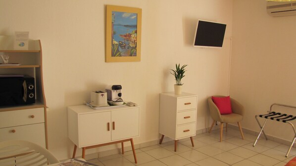 A small, well-lit room with a kitchenette, a single bed, a chair, a desk, and a wall-mounted TV. - Résidence Saint Michel (L'Île-Rousse)
