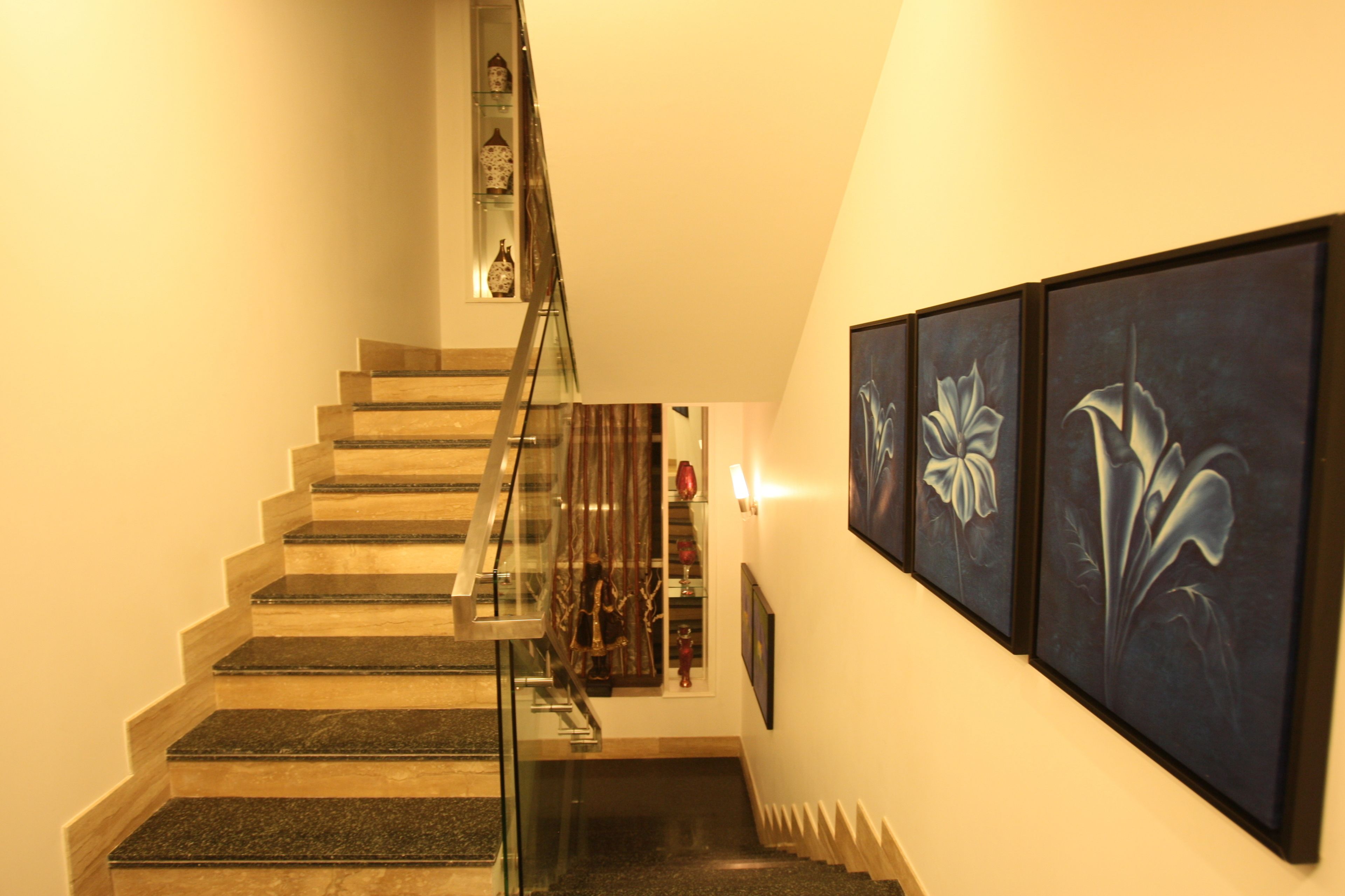 Un escalier avec des rampes en verre et un mur orné de tableaux encadrés.
