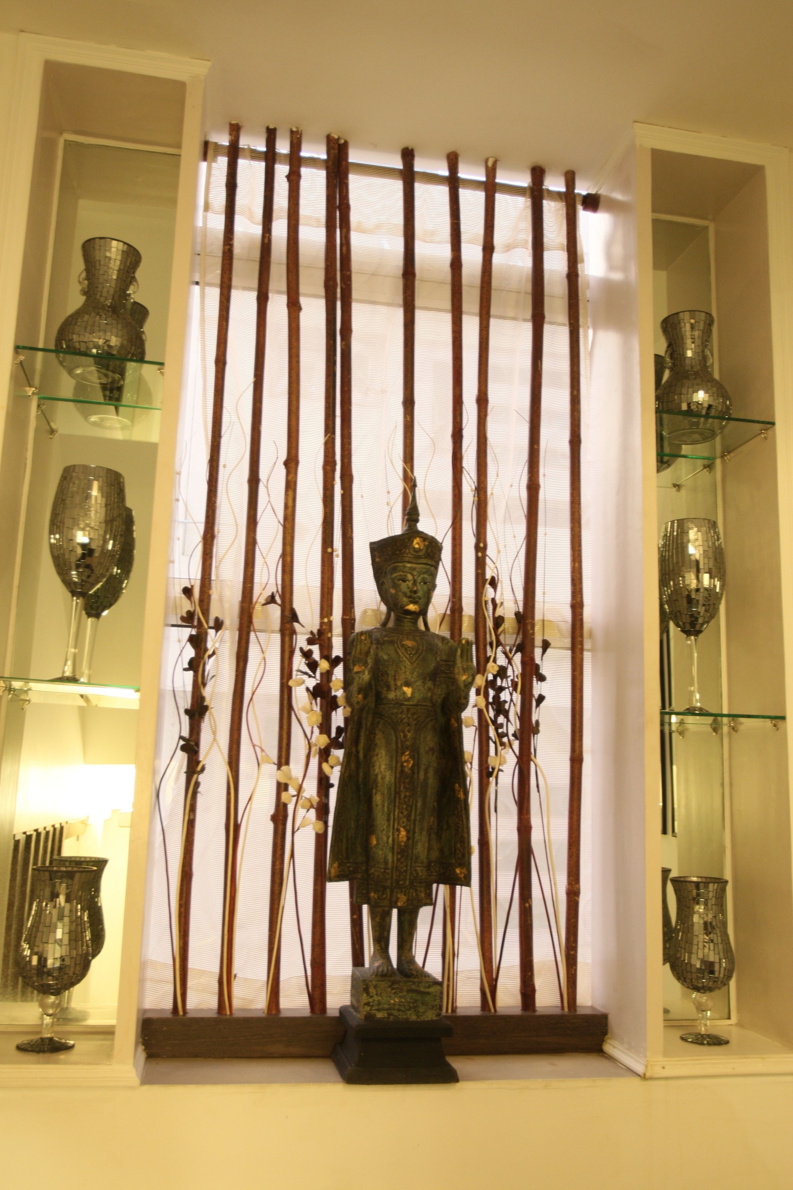 A statue in front of a bamboo screen, flanked by glass shelves with decorative vases.