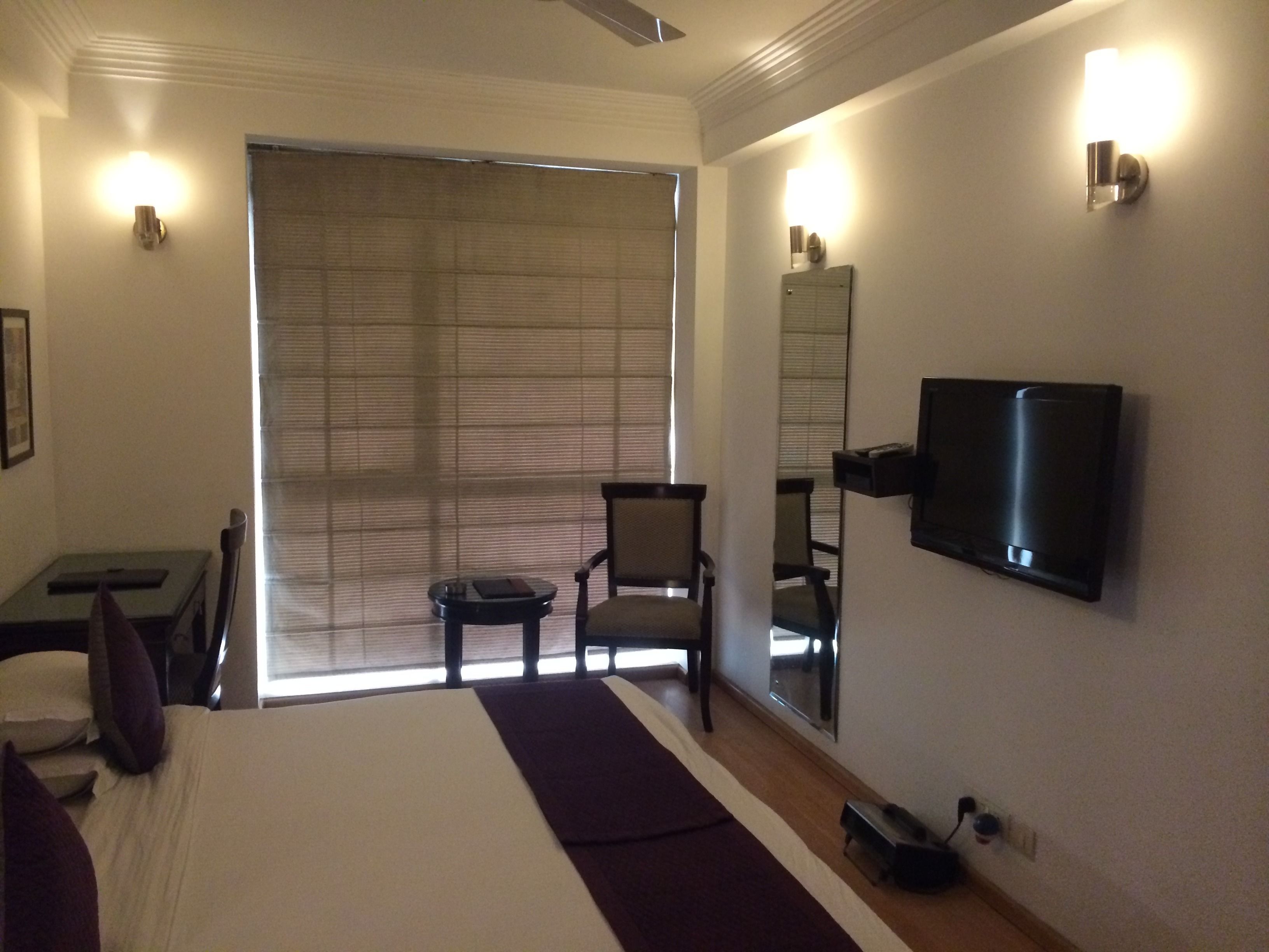 Ein Hotelzimmer mit Bett, Schreibtisch, Stuhl, Fernseher und einem großen Fenster mit Jalousien.