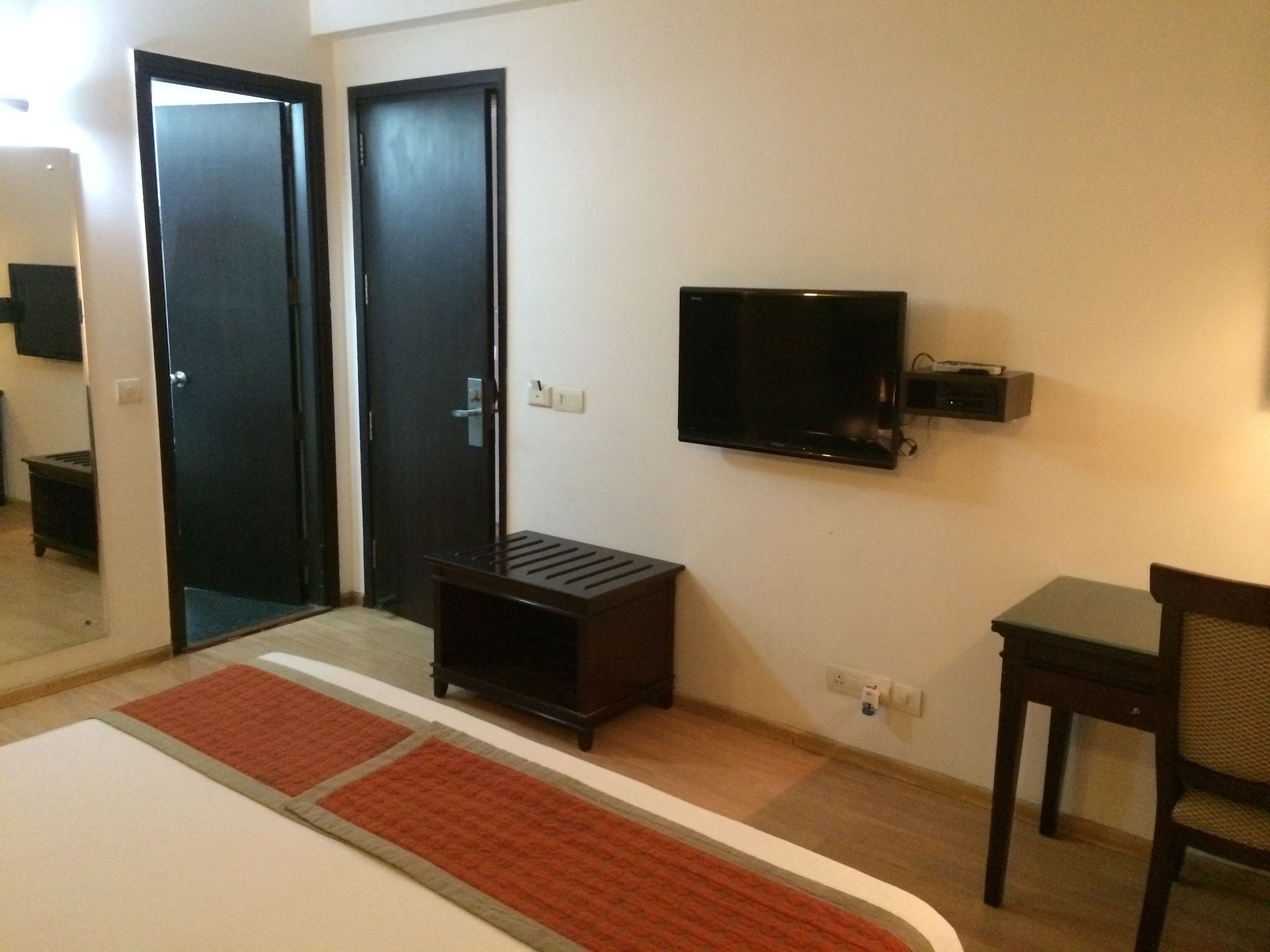 Habitación de hotel con una cama, televisión montada en la pared, una mesita y dos puertas.