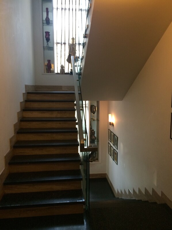 A staircase with wooden steps and a glass railing, leading to a landing with a small shelf displaying decorative items.