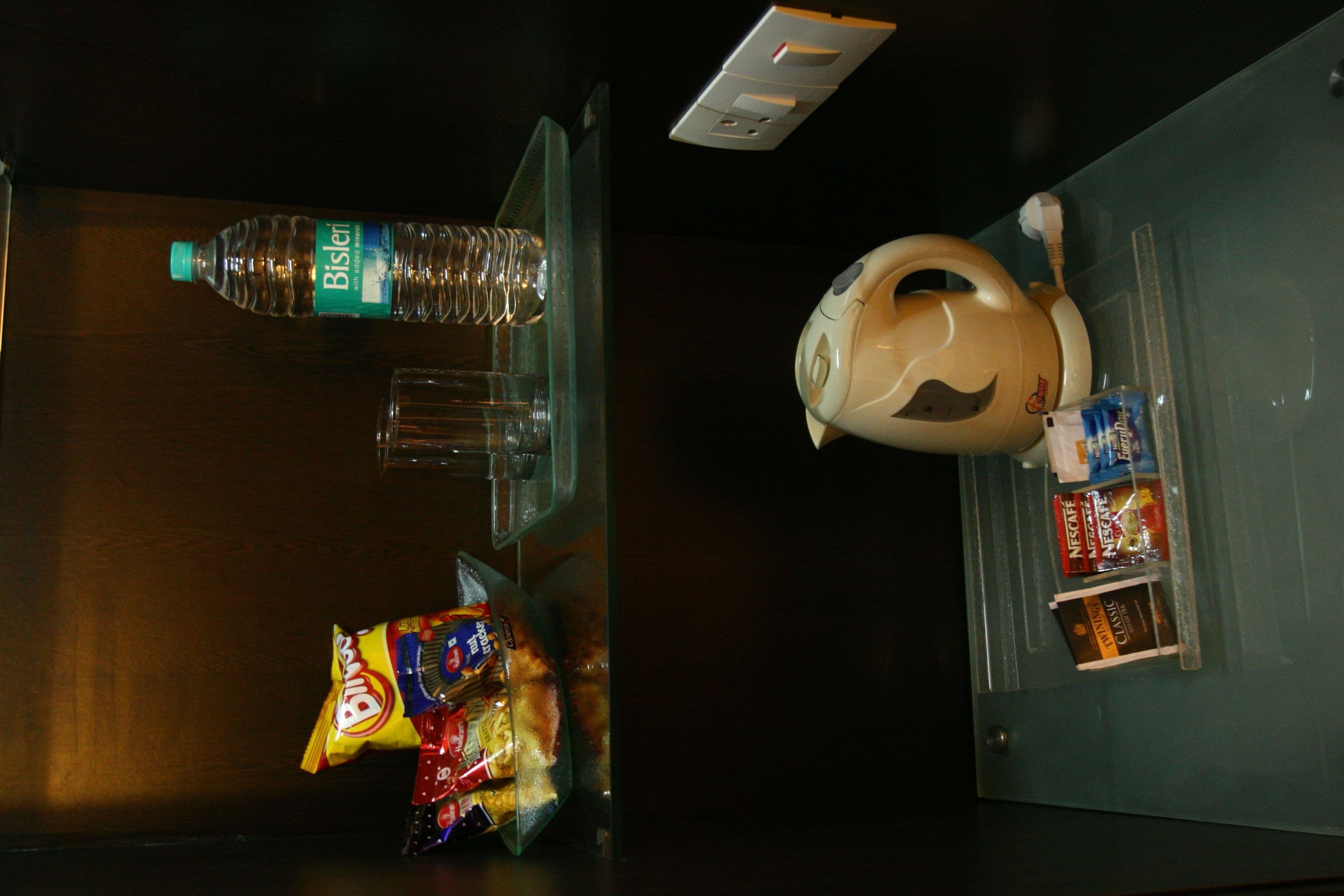 A minibar with a bottle of Bisleri water, a bag of snacks, and a coffee maker.