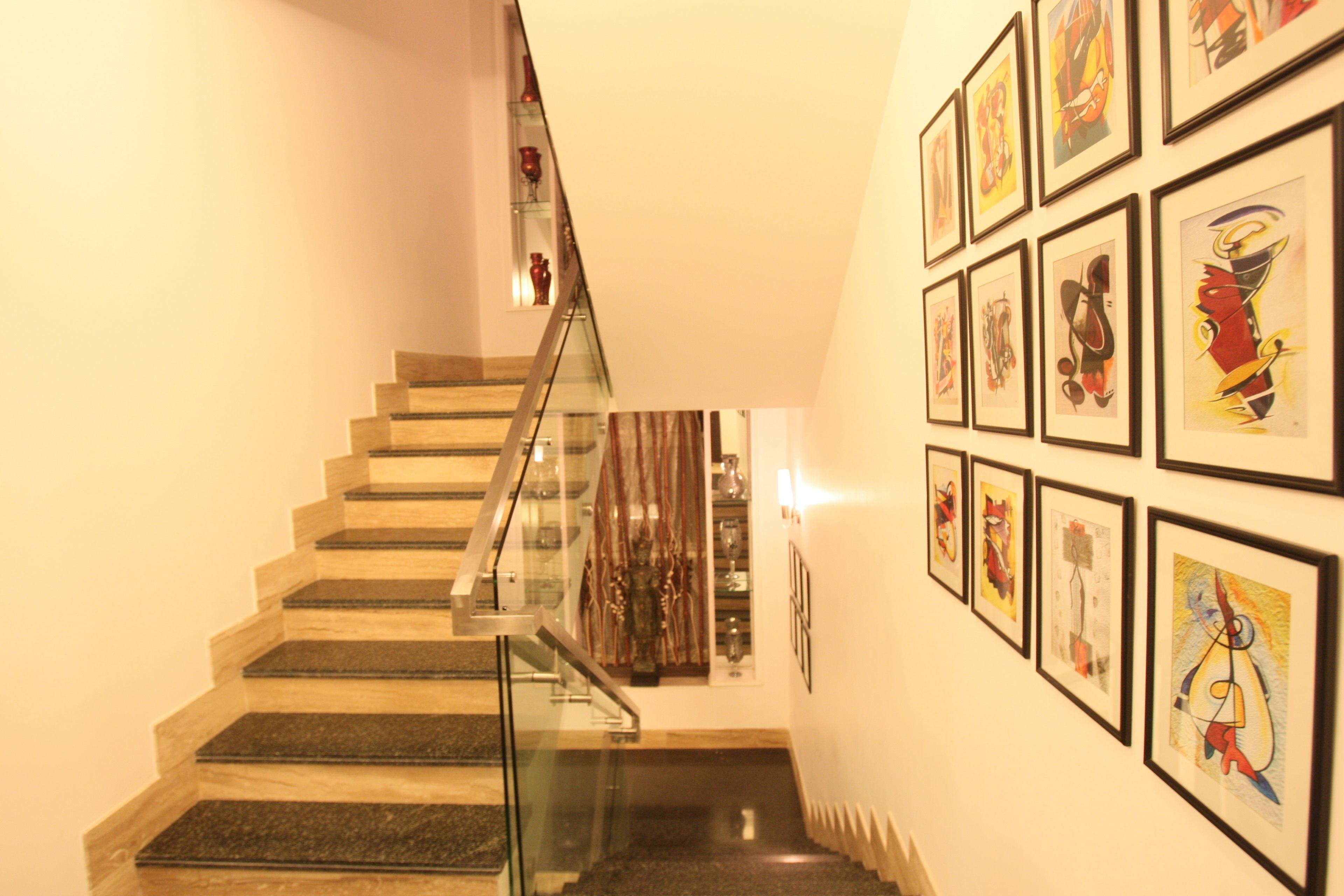 A staircase with glass railings leading to a landing with framed artwork on the walls.