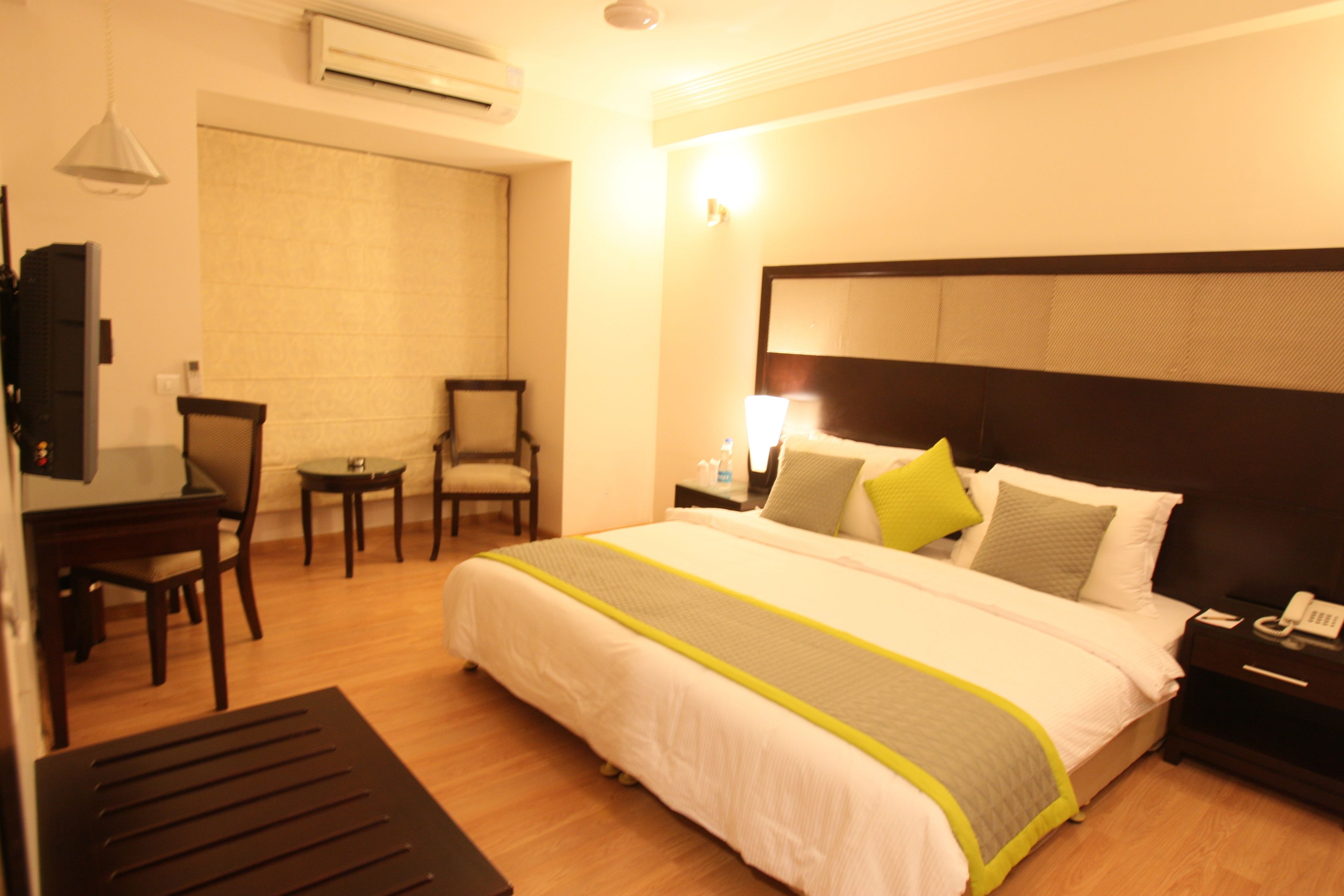 A hotel room with a large bed, a desk, two chairs, a bedside table with a lamp, and a telephone.