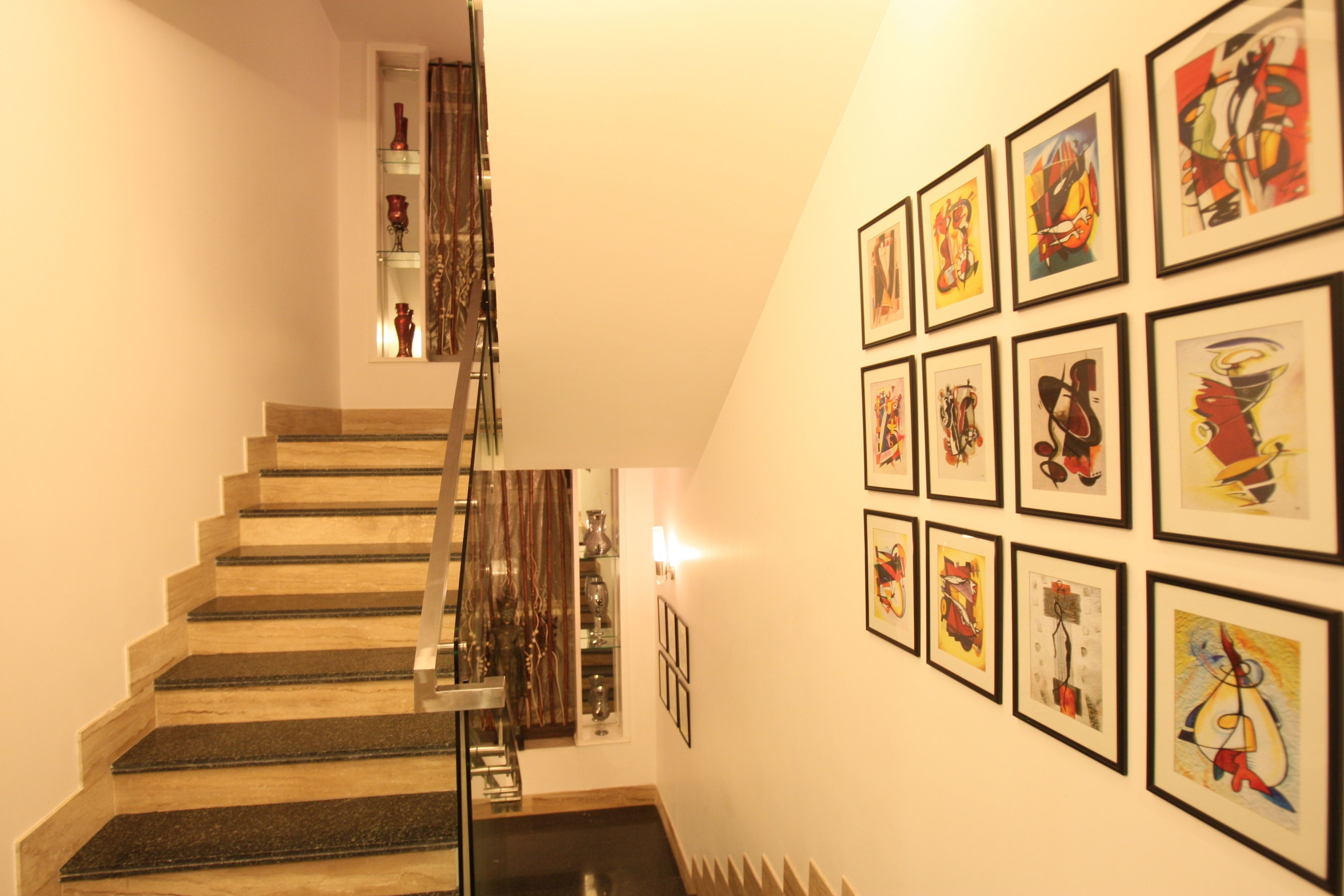 A staircase with a glass railing leading to a landing with a shelf of decorative items.
