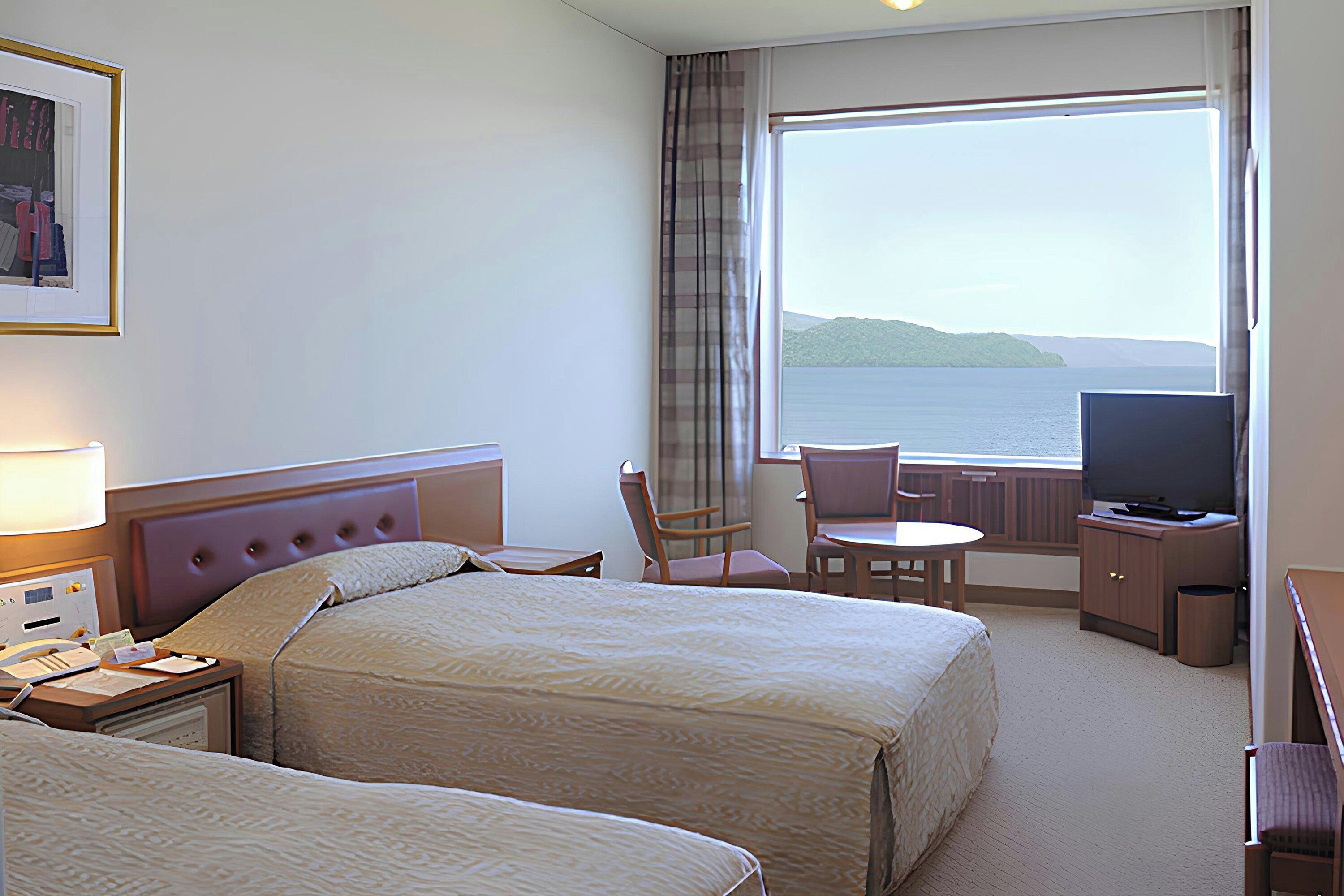 Ein Hotelzimmer mit zwei Betten, einem Fernseher, einem Schreibtisch und Meerblick.