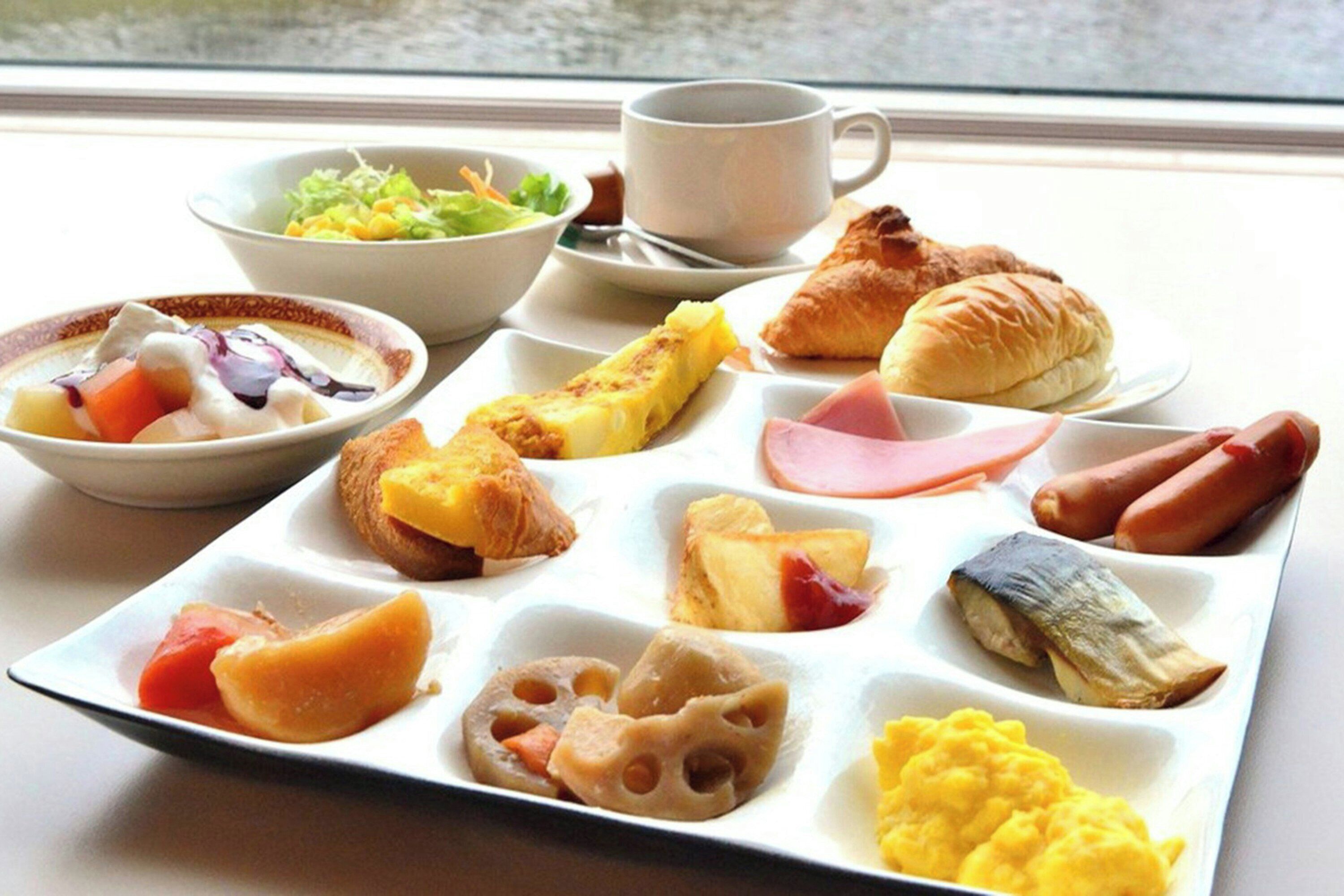 A breakfast tray with various foods, a cup, and a bowl of salad.