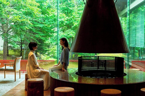 A circular seating area with a large, dark-colored grill in the center, surrounded by wooden stools. - Kussharo Prince Hotel (Teshikaga)
