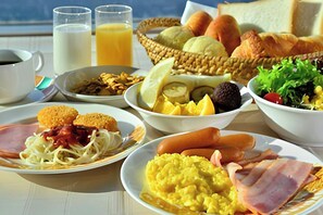 Una tavola imbandita per la colazione con uova strapazzate, bacon, salsicce e pane.